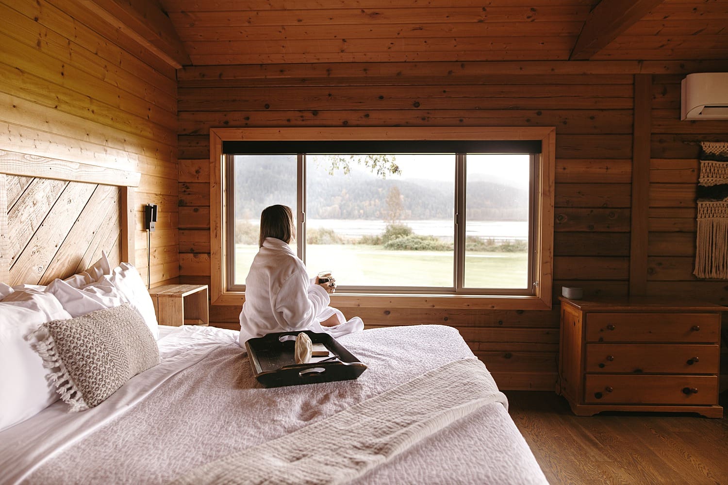 A woman sitting on a comfortable bed looking out the window at the view during a resort brand photo shoot